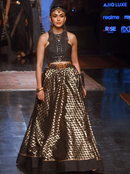 Mrunal Thakur looking powerful and elegant in a black and gold lehenga at Lakme Fashion Week. Her strong pose commands attention on the runway.
