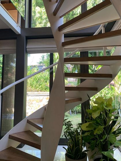 A white spiral staircase provides a light, sculptural connection between floors in this renovated home. Set against large glass windows, it allows uninterrupted views of the garden, making the journey through the house an experience of light and nature.
