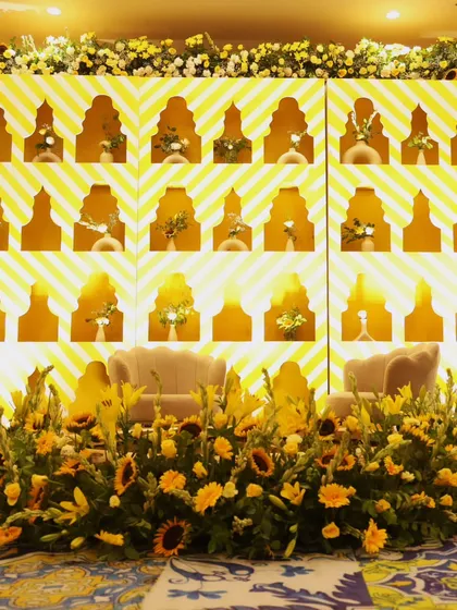 The main stage for the Haldi ceremony. A stunning backdrop with geometric patterns and niches for individual floral arrangements, all in radiant shades of yellow.