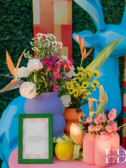 A close-up of a floral arrangement against the blue deer sculpture. The mix of tropical flowers like bird of paradise with daisies and roses creates a unique and eclectic bouquet.