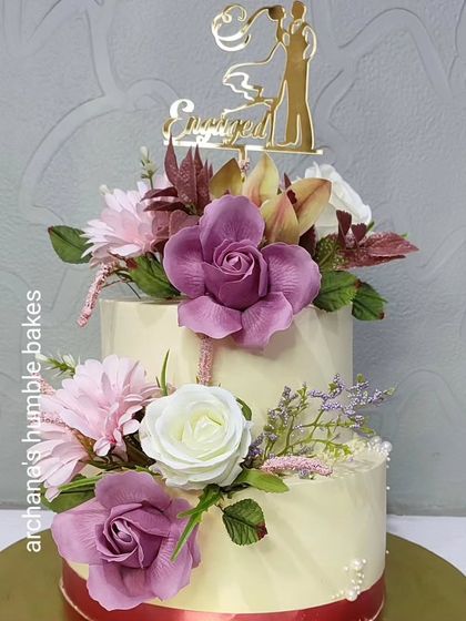 The full view of the two-tiered engagement cake with purple, pink, and white sugar flowers.