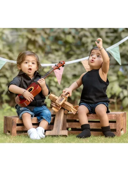 A duplicate of image 3, this photo shows the twins engaged in playful activities, one with a ukulele and the other with a toy plane, highlighting a fun, themed setup.