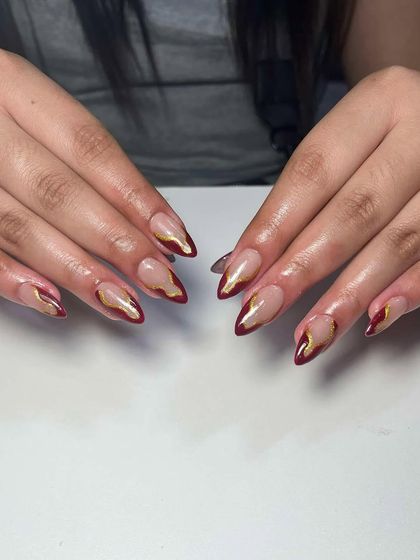 A dramatic design with a deep red and gold chrome abstract tip. This is a bold and artistic take on a French manicure.