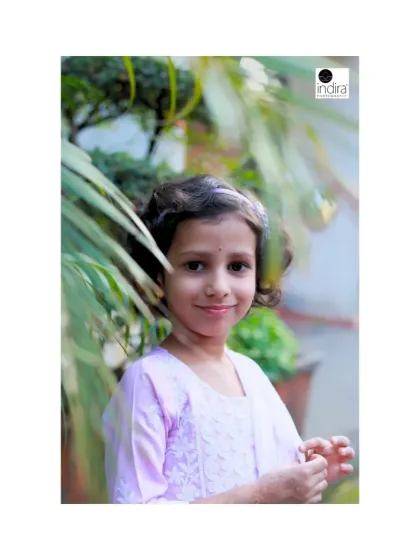 A lovely portrait of a young girl in a beautiful lavender outfit. The natural greenery in the background provides a perfect, soft frame for her sweet expression.