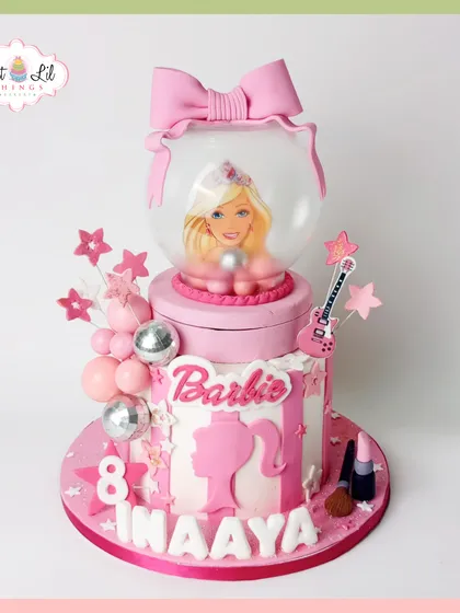 Come on Barbie, let's go party! This fabulous pink Barbie cake features a Barbie doll in a globe topper, along with glamorous details like a toy guitar and makeup, perfect for an 8th birthday.