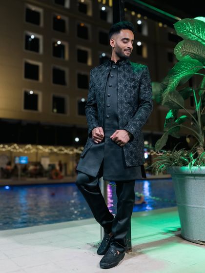 A stylish groom posing by the pool at his reception venue.