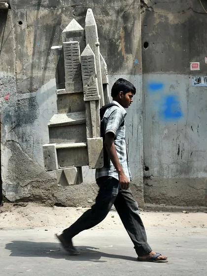 A boy carries a model of a city on his back, titled 'the weight of the city'. A symbolic image about the burdens and aspirations we carry.