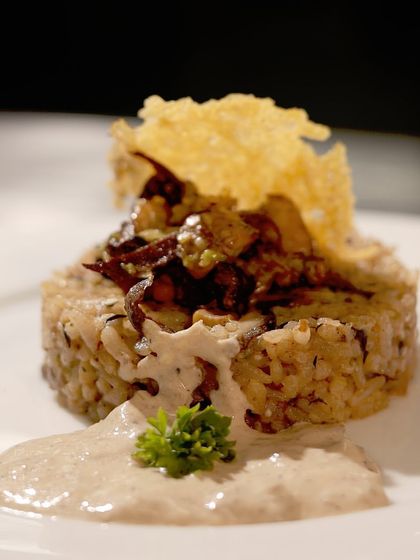 A sophisticated plated dish of mushroom risotto, topped with a crispy parmesan wafer. This dish showcases our ability to execute classic gourmet recipes with finesse.