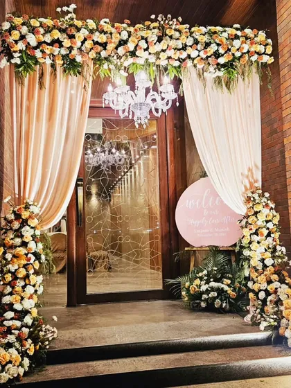A warm and inviting entrance with peach and cream florals and soft, flowing drapes. The chandelier adds a touch of glamour, welcoming guests to the Sangeet ceremony in style.