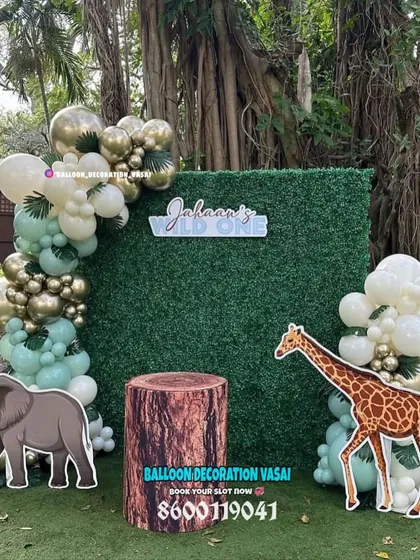 A "Wild One" jungle theme for an outdoor party. This setup features a grass wall backdrop, an elegant balloon garland, and realistic elephant and giraffe cutouts.