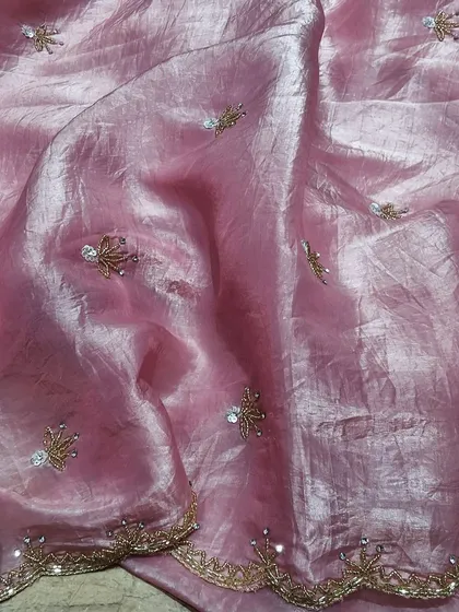 A close-up of a pink crush tissue saree with delicate, sparkling embroidery. The fabric has a lovely sheen and a soft, crushed texture that makes it unique and easy to drape.