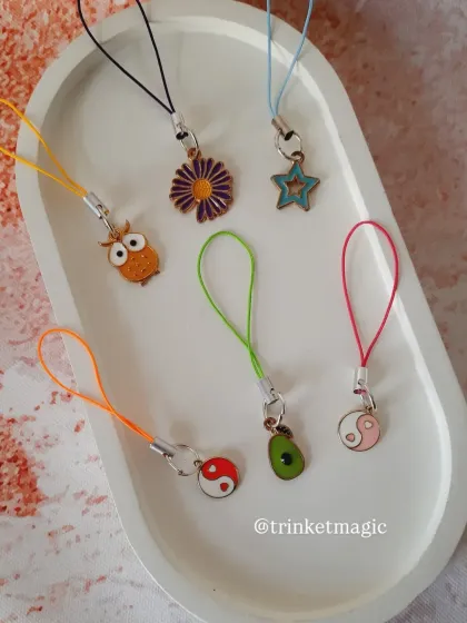 A collection of tiny phone charms with big vibes. This image includes a purple daisy, a blue star, an owl, an avocado, and yin-yang charms on colorful cords.