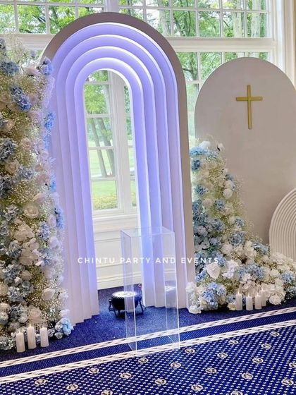 A stunning baptism stage decoration in blue and white. The setup features modern lighted arches and large floral arrangements for a grand and heavenly look.