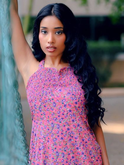 A beautiful outdoor portrait of a model in a pink floral dress. The composition uses a fence to create depth and frame the subject.