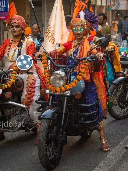 A woman in a stylish traditional outfit and sunglasses smiles as she sits on her motorcycle during the Gudi Padwa parade.