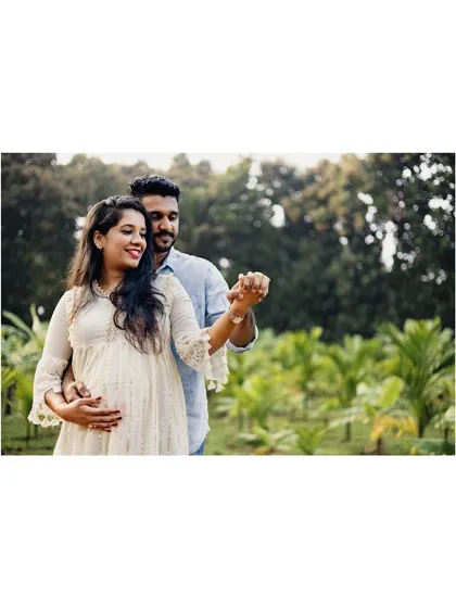 A romantic shot of an expecting couple dancing together in a lush, green field. This image captures a moment of joy and connection between the partners.