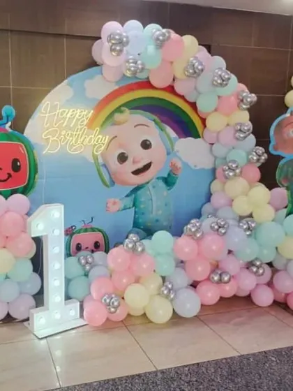 A Cocomelon first birthday setup with a pastel rainbow balloon arch. This popular theme is brought to life with character cutouts and a light-up number '1'.