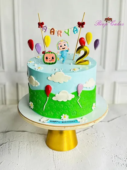 Joyful whimsy for a 2nd birthday. This vibrant cake is full of cheerful charm, featuring colorful balloons, fluffy clouds, and a cute Cocomelon character topper.