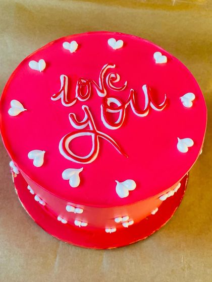 A bold and beautiful "Love You" cake in bright red, dotted with small white hearts. It's a sweet and simple way to celebrate your love.