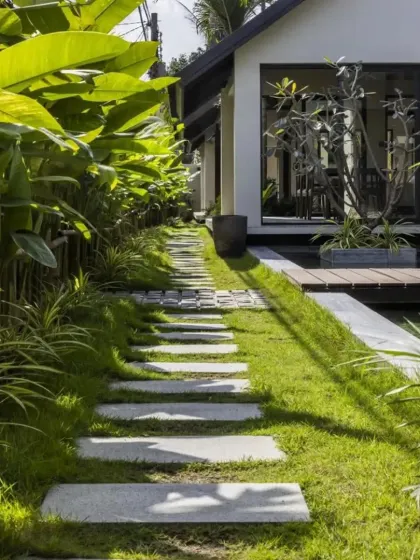 A rustic stone stepper path set in a lush lawn, leading towards a modern home. The path is surrounded by large-leafed plants, creating a tropical jungle feel.
