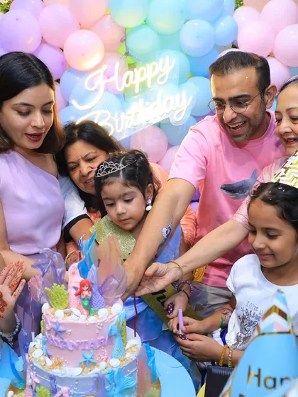 A happy family gathers around the birthday girl to help her cut her beautiful mermaid castle cake. It's a moment of shared celebration.