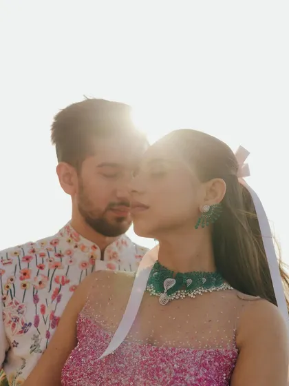 A sun-drenched, intimate portrait from a carnival-themed event. The close-up captures the couple's connection, with the bright light creating a dreamy, romantic haze.