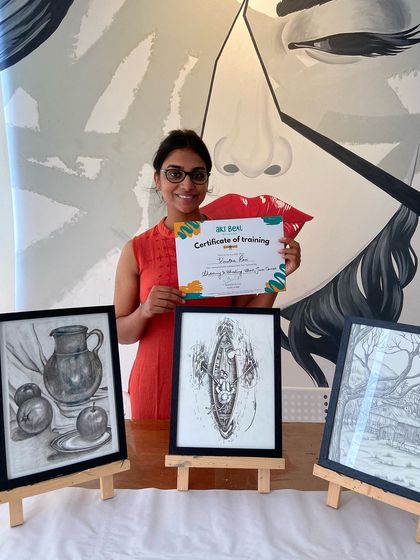 This student's hard work paid off. She's holding her certificate next to her three beautifully detailed sketches, including a still life and a landscape.