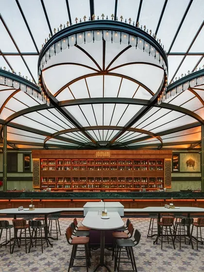 The heart of Jollygunj, the grand central bar. The custom-designed, canopy-like light fixtures are the focal point, illuminating the patterned floor tiles and extensive back bar. This element was crucial to the project's narrative, evoking the charm and grandeur of a bygone era.