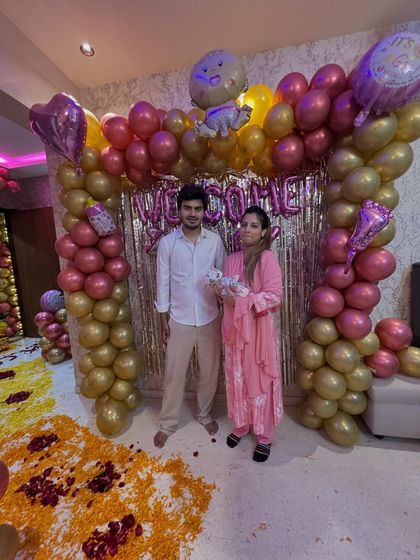 The happy new parents posing with their newborn in front of the 'Welcome Baby' decoration I set up in their home.