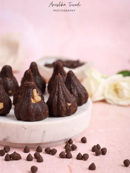 Chocolate-walnut modaks on a clean, modern pedestal. The pink background adds a contemporary twist to the styling of this traditional festive sweet.