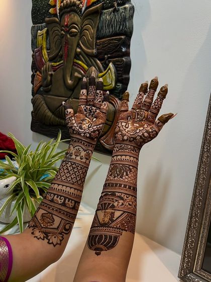 A full-arm bridal design with a mix of traditional motifs, captured against a backdrop of Ganesha art.