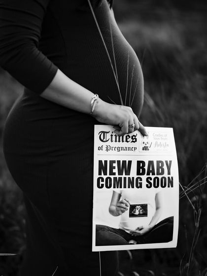 A classic black and white shot of the mom-to-be holding "The Times of Pregnancy" newspaper, with her beautiful baby bump as the main subject.