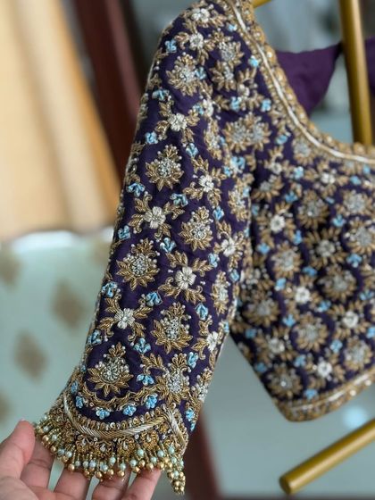 A hand holding the sleeve of the purple velvet blouse, showing the scale and density of the embroidery.