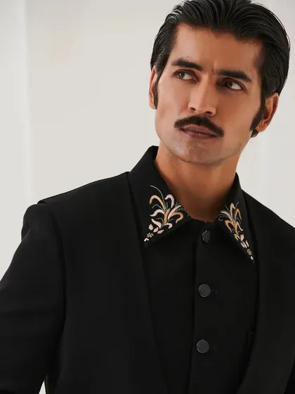 A close-up on the embroidered collar of the Nazaakat bandhgala. The gold and white threadwork provides a touch of royalty against the black fabric.