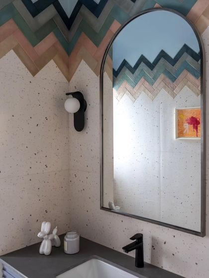 The attached bathroom continues the playful theme with a bold chevron pattern of colorful tiles. The arched mirror and simple wall sconce add a touch of elegance to the fun design.