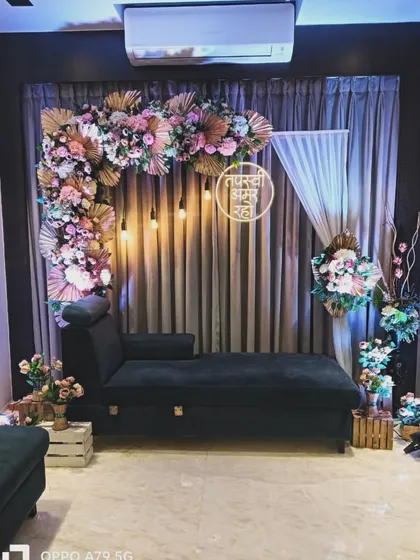 An intimate home engagement setup. I created a corner floral arch with pampas grass and a neon sign with the couple's initials in a ring, all set against a simple curtain backdrop.