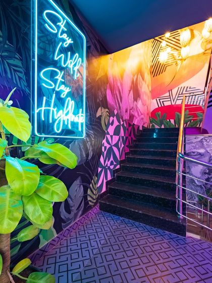 Another angle of the staircase, showing how the bright green of the plant contrasts with the neon sign and dark, leafy wallpaper. Every detail is curated to enhance the wild, tropical theme.