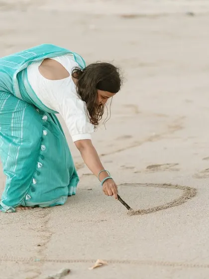 A simple, creative act of drawing a heart in the sand, symbolizing the timeless and personal nature of their love story.