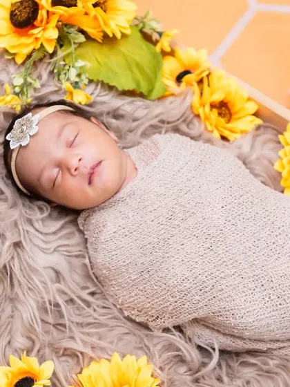 A peaceful newborn baby, swaddled snugly in a beige wrap, sleeping in a wooden crate adorned with bright yellow sunflowers.