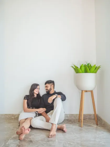 A simple and sweet moment of the couple sitting on the floor against a white wall, holding hands. This minimalist shot focuses entirely on their connection.