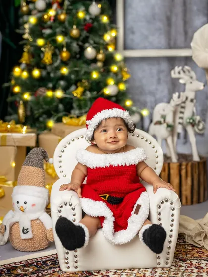 Dressed as a little Santa, this baby sits comfortably in a mini armchair, embodying the joy and wonder of the holiday season.