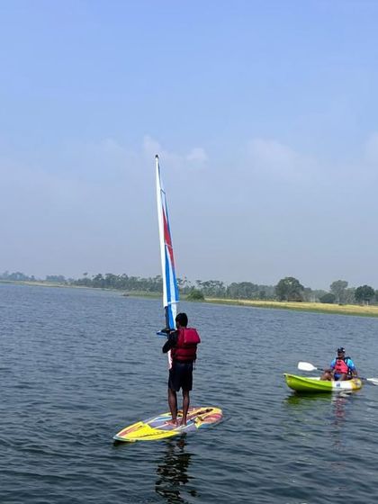 A windsurfer stands tall on his board, practicing his balance and control of the sail on a calm day.