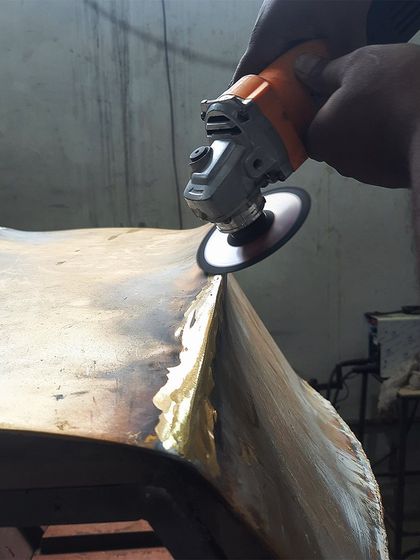 A behind-the-scenes look at our workshop, where a craftsman is carefully grinding and shaping a bent brass sheet. This is part of the process for creating a custom furniture piece.