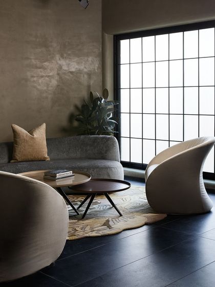 A different perspective of the grey curved sofa, showing its elegant form against the textured, lime-washed walls. The space feels intimate and enclosed, perfect for showcasing a cozy living setup.