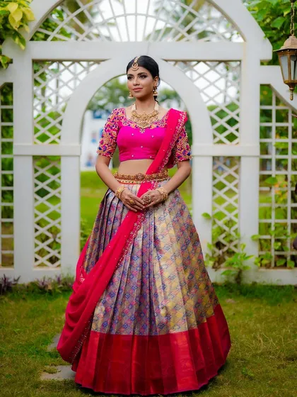 A full-length bridal portrait is essential to showcase the entire look. Here, the bride's magnificent Kanjeevaram half saree stands out against the soft garden setting, showing the grandeur of her wedding day attire.