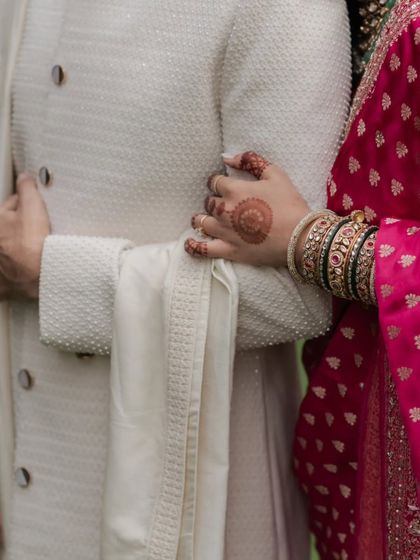 A detail shot symbolizing our commitment. The bride's henna-adorned hand on the groom's arm represents the stories we are trusted to tell.