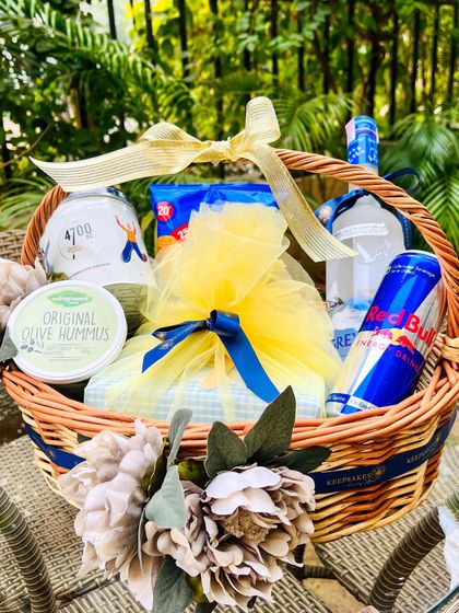 This birthday basket was envisioned by the client to include all the recipient's favorite things. It features Grey Goose vodka, Red Bull, hummus, and snacks, all tied together with a beautiful gold and blue theme.