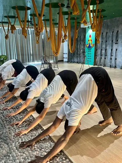 Teacher trainees practicing Adho Mukha Svanasana (Downward-Facing Dog) on a pebble-textured floor, which provides acupressure benefits. We explore every detail to enhance the practice.