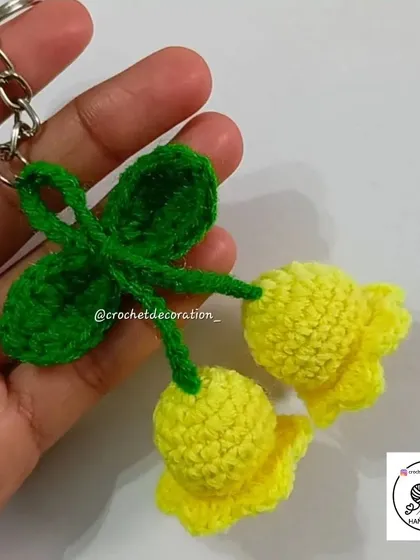 A handmade crochet keyring featuring two yellow lily of the valley flowers and a leaf. It's a beautiful and practical little accessory.