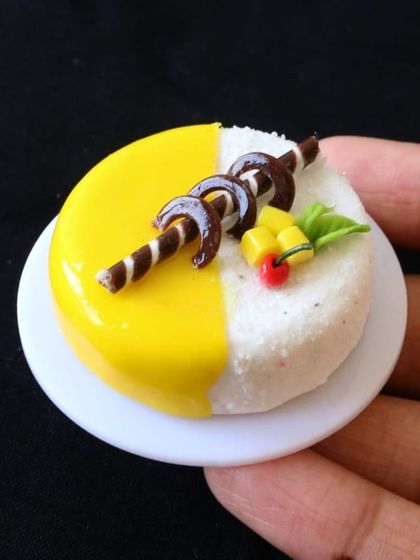 A miniature mango cake, with a bright yellow glaze and delicate chocolate decorations.